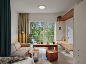 Living area of a fully furnished studio apartment at Fellows Jaselská with large windows overlooking Brno.
